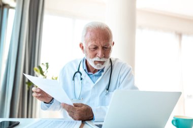 Kıdemli Doktor Laptop 'ta Tıbbi Raporları İnceleme, Sağlık Hizmetleri Profesyonel Danışmanlık Online, Tıbbi Kayıt Analizi. Steteskoplu olgun bir doktor hasta belgeleriyle ofiste çalışıyor..