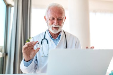 Video Çağrısında Olgun Doktor Tutucu Aşı Viyatı Laptop Kameraya Tıbbi Profesyonel İlaç Gösterimi. Kıdemli hekim teletıp oturumunda aşılama ya da tedaviyi açıkladı.