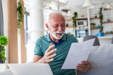 Son sınıf öğrencisi Bill 'i ya da Evdeki Belge' yi incelerken, Mutlu Olgun Erkek Okuma Kağıtları Kanepe 'de dizüstü bilgisayar kullanırken. Finans veya sağlık sigortasını yöneten yaşlı kişi, iç mekanda olumlu sonuçlar doğurur.