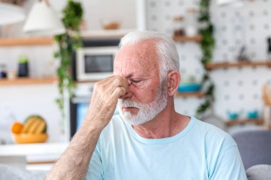 Sinüs ağrısı olan son sınıf öğrencisi burun köprüsüne dokunuyor. Yaşlı erkek baş ağrısı, alerji ya da evde baskıdan muzdarip. Sağlık ve tıp konsepti. Oturma odasında gözleri kapalı yorgun bir insan..