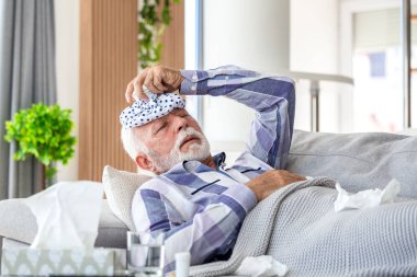 Başı ağrıyan son sınıf öğrencisi buz torbasıyla kanepede yatıyor. Hasta, yaşlı bir erkek migren ya da evde yüksek ateş geçiriyor. Sağlık ve tıp konsepti. Soğuk algınlığı veya grip belirtileri gösteren kişiler dinleniyor.