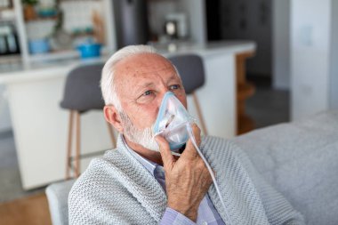 Evde oksijen maskesi kullanan kıdemli bir adam. Solunum problemleri olan yaşlı bir erkek hasta nebulizatörle nefes alıyor. Sağlık, astım ve KOAH tedavi konsepti. Tıbbi ekipmanlı emekli adam..