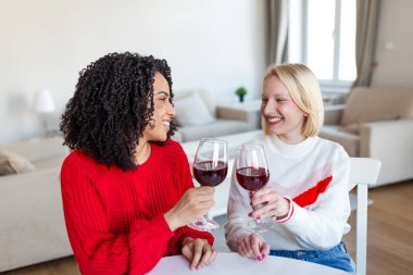 Evde kırmızı şarapla kadeh kaldıran iki farklı kadın. Oturma odasında kutlama yapan arkadaşlar. Neşeli Bayan Arkadaşlar Akşam Yemeği Partisi ya da Hafta Sonu Eğlencesi İçin Şarap İçiyor.