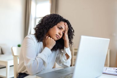 İş stresi. Başı ağrıyan yorgun bir kadın, zihinsel yorgunluk sorunu olan insanlar, sağlık sigortası ve ilaç konsepti. Çekici Afrikalı Amerikalı kadın masada oturuyor ve dizüstü bilgisayarına bakıyor..