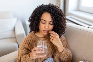 Evde ilaç alıyordum. Hap yutan hasta kadın, sağlık sorunu olan insanlar, sağlık sigortası ve ilaç konsepti. Çekici Afrikalı Amerikalı kadın elinde bir bardak su ve tıbbi kapsül tutuyor..