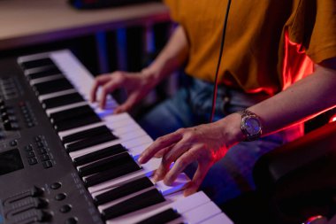 Eller piyano çalıyor. Klavye müzisyeni, müzik prodüksiyonu konsepti. Yaratıcı sanatçı parmakları atmosferik kırmızı ve mavi neon ışıklı ev stüdyosundaki MIDI kontrol anahtarlarında. Ellerin görüntüsünü kapat.
