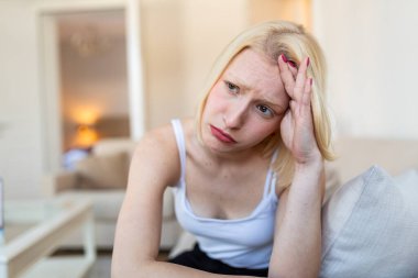 Baş ağrısı ve migren. Başı ağrıyan üzgün bir kadın, stresi ve yorgunluğu olan insanlar, sağlık sigortası ve ilaç konsepti. Çekici sarışın kız kanepede oturuyor ve alnını eliyle tutuyor..