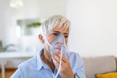 Üst düzey kadın evde solunum terapisi için oksijen maskesi kullanıyor. Kısa gri saçlı, nebulizör maskeli olgun bir bayan. Sağlık, astım, zatürree ve solunum problemi olan tıp konsepti.