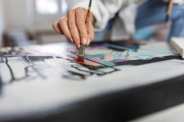 Bir kadın sanatçının elinin, parlak bir ev stüdyosunda, sanatsal bir süreçte, yaratıcı bir proje üzerinde çalışan, fırçayla soyut bir tuvale canlı kırmızı boya sürerken yakın çekimi..