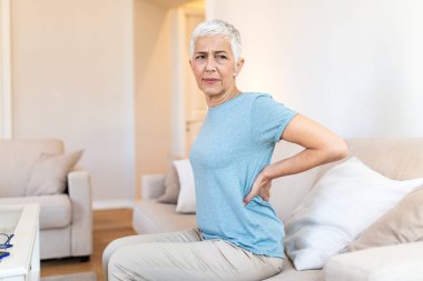 Sırt ağrısı. Sırtı ağrıyan olgun bir kadın, vücut kası sorunu olan insanlar, sağlık ve tıp konsepti. Yaşlı kadın kanepede oturuyor ve elleriyle sırtına acı veriyor. Omurga yaralanması.