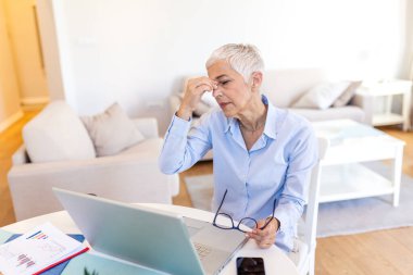 Göz yorgunluğu. Baş ağrısı olan olgun bir kadın, vücut kası sorunu olan insanlar, sağlık ve tıp konsepti. Yaşlı bayan masada oturuyor ve burnunda acı dolu bir köprüyü tutuyor. Görüş sorunu belirtileri