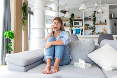 Üzgün kadın kanepede ağlıyor ve peçeteyle gözyaşlarını siliyor. Akıl sağlığı, depresyon ve yalnızlık kavramı. Mutsuz kız oturma odasında yalnız oturuyor, hayal kırıklığına uğramış ya da kalbi kırılmış..