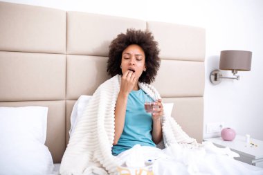 Yatağında su ile ilaç yutan hasta bir kadın. Sağlık ve tıp konsepti. Aspirin ya da vitamin alan genç bir kadın. Grip tedavisi, ilave ve ve evde bakım..