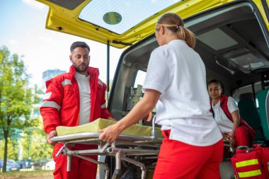 Ambulansın yanında sedye taşıyan sağlık görevlileri. Sağlık görevlileri ambulans arabasını sedyeyle çıkarıyorlar.