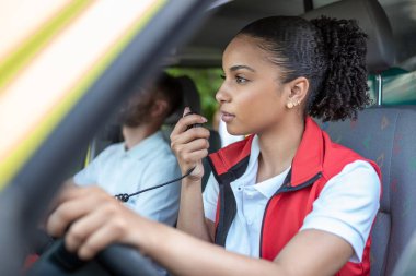 Genç bir kadın ambulansla çağrıya cevap veriyor. İş arkadaşıyla birlikte. Koruyucu sağlık üniforması giyiyorlar.
