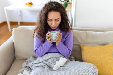 Closeup view of young Asian woman with cup of hot drink at home, covered with blanket. People, drinks and leisure concept - young woman with cup of tea or coffee at home