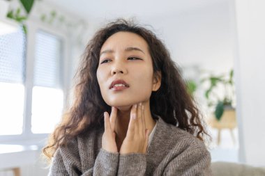 Close up of young Asian woman rubbing her inflamed tonsils, tonsilitis problem, cropped. Woman with thyroid gland problem, touching her neck, girl has a sore throat