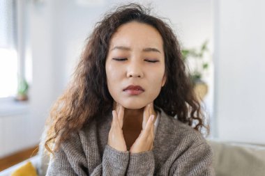 Close up of young Asian woman rubbing her inflamed tonsils, tonsilitis problem, cropped. Woman with thyroid gland problem, touching her neck, girl has a sore throat