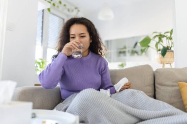 Asian ill sick woman taking painkiller medicine to relieve stomachache pain sit on bed in the morning. Sick woman lying in bed with high fever. Cold flu and migraine.