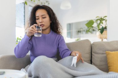 Asian ill sick woman taking painkiller medicine to relieve stomachache pain sit on bed in the morning. Sick woman lying in bed with high fever. Cold flu and migraine.