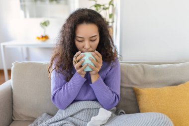 Closeup view of young Asian woman with cup of hot drink at home, covered with blanket. People, drinks and leisure concept - young woman with cup of tea or coffee at home