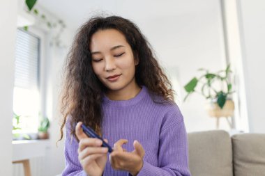 Parmak üzerinde mızrak kullanan Asyalı kadın. Oturma odasında kan şekeri testi yapan bir kadın..