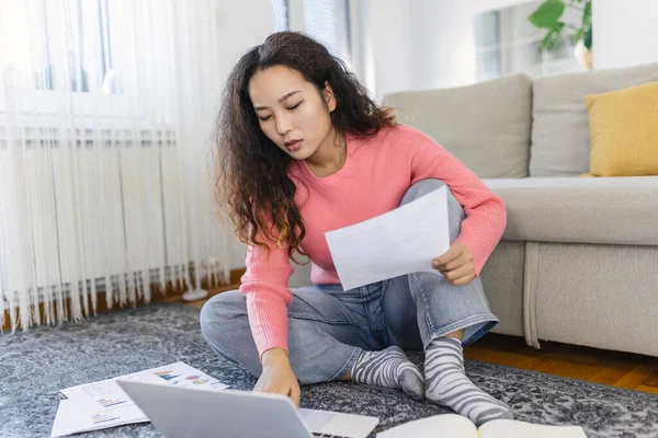 Positive young Asian woman freelancer working on netbook on the floor at comfortable home. Beautiful young business woman working on laptop.Freelancer connecting to internet