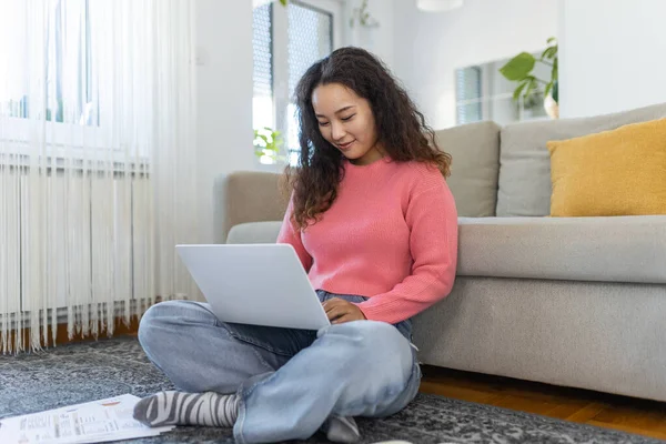 Asian woman sitting with computer on sofa, studying at home, e-learning and remote freelance job concept