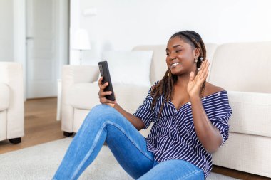 Evdeki kanepede dinlenirken cep telefonu kullanan genç bir kadının fotoğrafı.