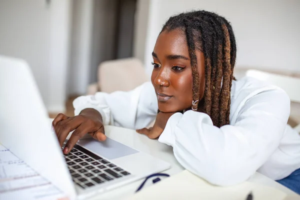 Uzak iş, teknoloji ve insan konsepti - Covid-19 sağlık krizi sırasında merkez büroda çalışan dizüstü bilgisayarı ve kağıtları olan genç Afrikalı iş kadını.