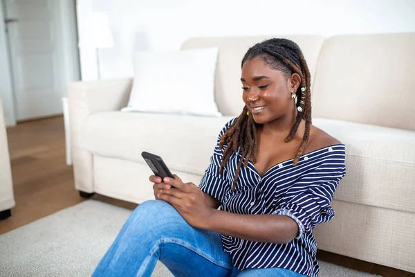 Evdeki kanepede dinlenirken cep telefonu kullanan genç bir kadının fotoğrafı.