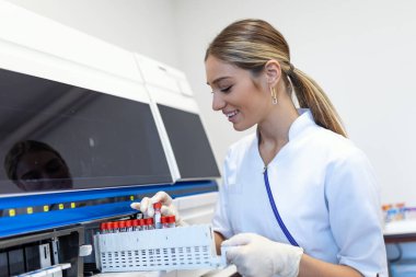 Portrait of a young female laboratory assistant making analysis with test tubes and analyzer machines sitting at the modern laboratory
