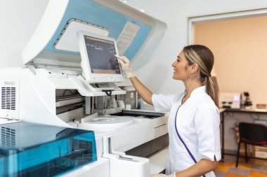 Portrait of a young female laboratory assistant making analysis with test tubes and analyzer machines sitting at the modern laboratory