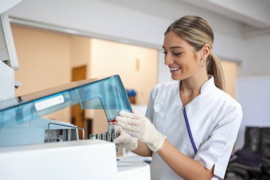Female laboratory assistant making analysis with test tubes and analyzer machines sitting at the modern laboratory, lab tech loading samples into a chemistry analyzer