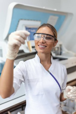 Biyokimya bölümündeki genç doktoru kapatın. Genetik materyal numunesiyle test tüpünü inceleyin ve tutun. Steril laboratuvarda kimya araştırmacısı mikrobiyoloji sıvısını test etmek için modern teknolojiyi kullanıyor.