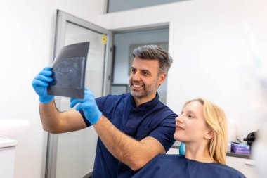 Doktor hastasıyla konuşuyor ve radyografi öğretiyor. Diş hekimi, dişçisi röntgen taramasını okurken dişçi koltuğunda oturan kadın konsepti.