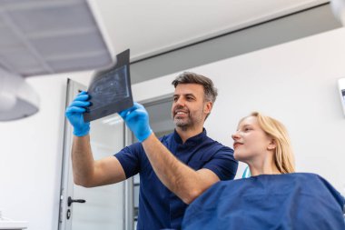 Doktor hastasıyla konuşuyor ve radyografi öğretiyor. Diş hekimi, dişçisi röntgen taramasını okurken dişçi koltuğunda oturan kadın konsepti.