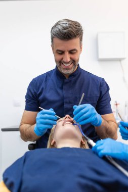Image of pretty young woman sitting in dental chair at medical center while professional doctor fixing her teeth