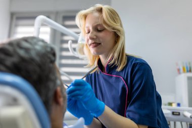 Kadın dişçi mavi eldivenlerle diş dolgusunu tedavi ediyor. Diş hekimi kliniğinde tedavi görüyor. Halk, tıp, stomatoloji ve sağlık hizmetleri kavramı