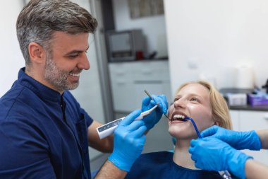 Tıp merkezindeki dişçi koltuğunda oturan tatmin olmuş genç bir kadın resmi.