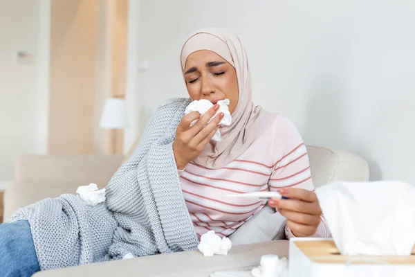 Arap kadın grip olmuş ve termometre kullanıyor. Rhinitis hastası, tesettürlü bir kadının burnu akıyor. Kanepede uzanmış, termometrede sıcaklığa bakan hasta bir kadın..