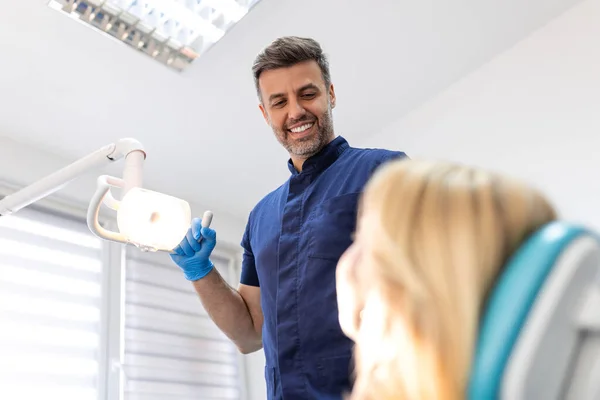 Erkek dişçinin, dişçi sandalyesinde oturan hastanın kafasının üstündeki yansıtıcı ışıkları ayarlarken düşük açılı görüntüsü. Diş hekimi işe başlamadan önce projektörü ayarlar