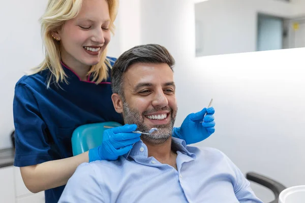 Diş hekimindeki randevusu sırasında dişlerini muayene eden genç bir dişçi. Hastanın ağzının yanında diş aletleri tutan bir doktorun elleri. Sağlıklı diş ve ilaç konsepti