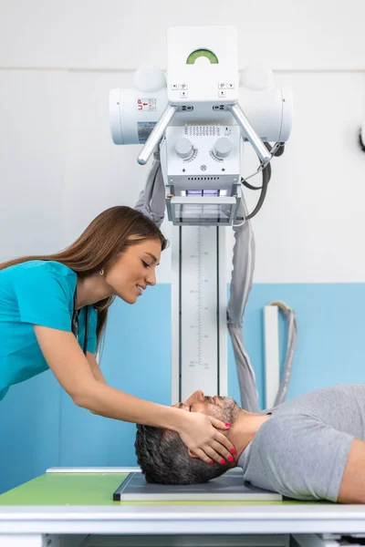 Kadın hemşire kolunu ya da elini taramak için modern röntgen cihazını ayarlarken erkek hasta oturuyor.