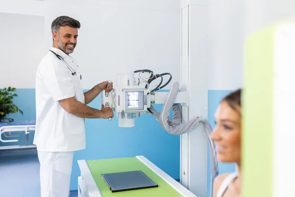 Radyolog makineyi kadın hastaya röntgen için ayarlıyor. Radyolog ve hasta röntgen odasında. Klasik tavana monte edilmiş röntgen sistemi. Tıbbi ekipman