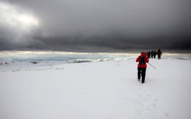 Dağlarda karla kaplı bir grup dağcı yürüyor.