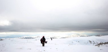 Dağlarda karla kaplı bir grup dağcı yürüyor.