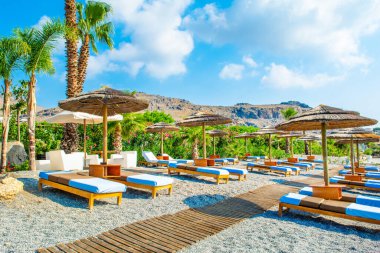 Yunanistan 'ın Rodos adasındaki Akdeniz kıyısında güneşli yataklı ve saman şemsiyeli güzel kayalık plajlar