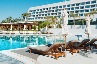 Limasol, Kıbrıs - 19 Mayıs 2021: Lüks modern otelin havuz alanı, palmiye ağaçları ve tropikal bitkilerin gölgesinde güneşli yataklar