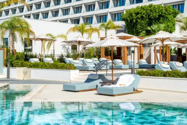 Limasol, Kıbrıs - 19 Mayıs 2021: Lüks modern otelin havuz alanı, palmiye ağaçları ve tropikal bitkilerin gölgesinde güneşli yataklar